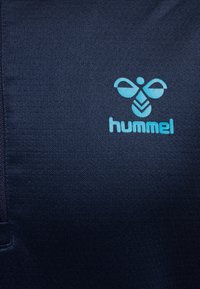 Granatowa tkanina o fakturowanym wyglądzie, z jasnoniebieskim logo "hummel" i stylizowanym wzorem pszczoły w lewym górnym rogu.