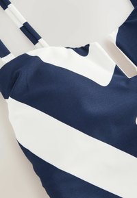 Tumesinine ja valge tank-top, mis on kaunistatud julgete diagonaalsete triipudega. Valmistatud siledast kangast, millel on õhukesed rihmad ja ümmargune kaelus.