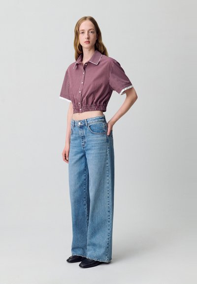 Camisa corta de cuadros rojos y blancos con mangas cortas y elástico en el dobladillo, combinada con vaqueros de mezclilla azul claro de pierna ancha y zapatos negros.