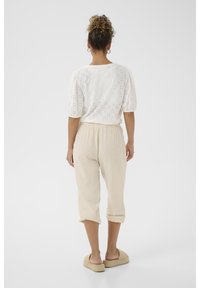 Outfit da donna caratterizzato da una blouse bianca in pizzo con maniche a sbuffo e pantaloni in lino beige a vita corta, abbinati a sandali espadrillas color nocciola.