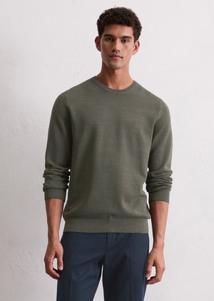 Green knitted sweater with long sleeves and a round neckline. Features a textured surface and ribbed cuffs and hem. Worn with dark pants.