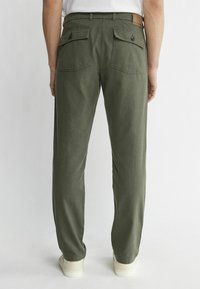 Gröna, lätta byxor med rak skärning. Har två bakfickor med lock och knappar, och en läderlapp i midjan.