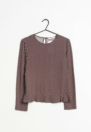 Long-sleeve top in a red and black circular dot pattern, featuring a round neckline, back keyhole detail, and subtle pleated hem.