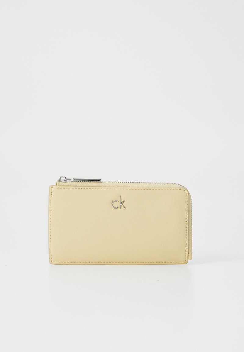 Portefeuille en cuir jaune avec une texture lisse, fermeture zippée et armatures en métal argenté. Présente un logo en relief discret à l'avant.