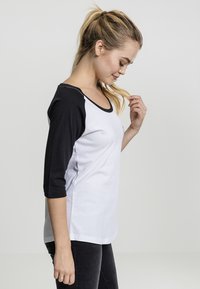 Black and white three-quarter sleeve shirt, featuring a round neckline and a relaxed fit. Made from soft cotton material, minimalistic design.