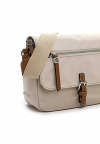 Beige Stoff-Umhängetasche mit breitem beigem Gurt, braunen Leder-Reißverschlussanhängern, Schnallendetail auf der Vorderseite und silbernen Metallakzenten.