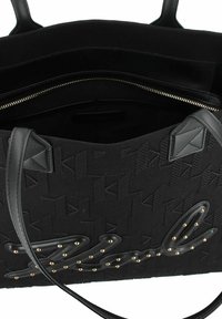 Zwarte tas gemaakt van textuurstof met debossed patronen, leren accenten en gouden studs op een cursieve logo. Interieur met zichtbare ritszak.