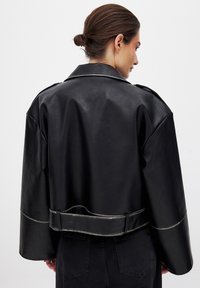 Svart faux läderjacka med en kortad design, bred krage och silverdetaljer. Har långa ärmar och midjebälte.