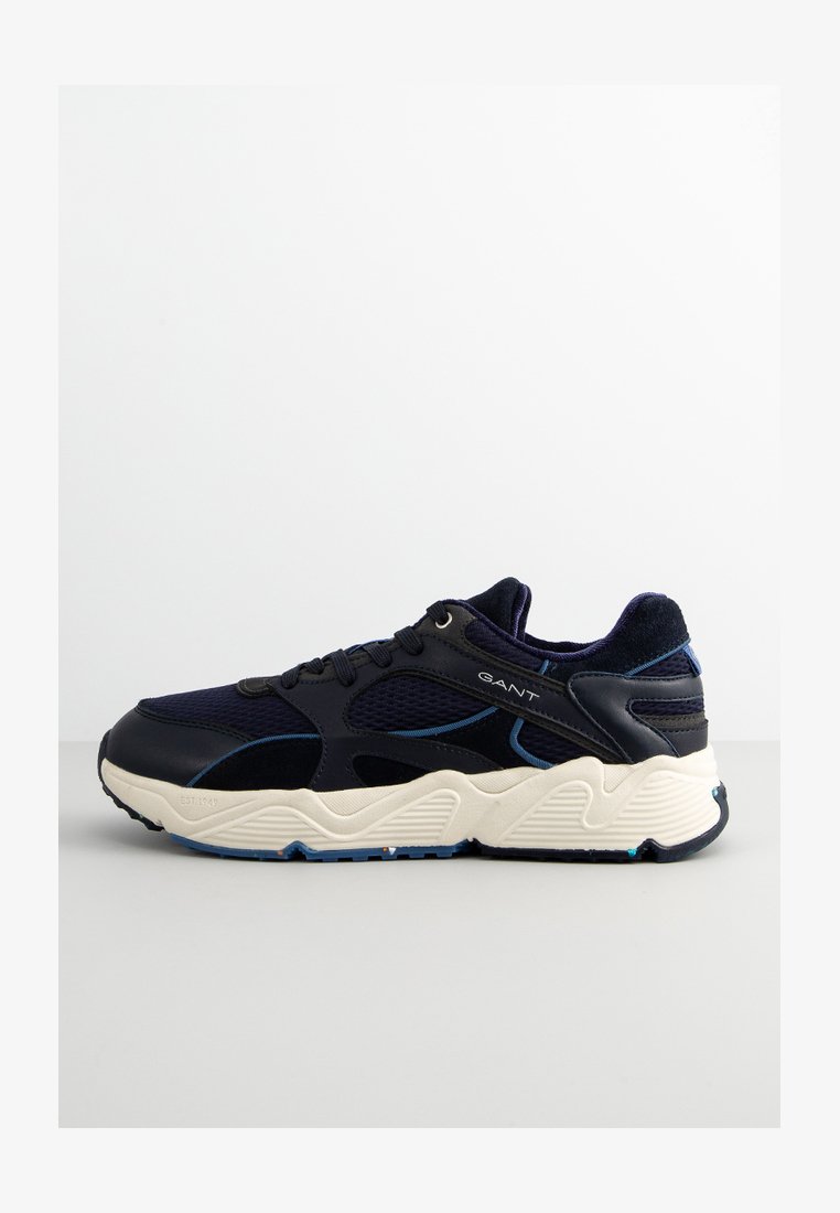 Navy blue athletic sneaker with mesh and suede materials, chunky white midsole, blue accents, and a textured sole for grip.