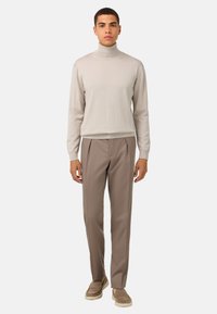 Ljusbeige polotröja, stickad textur, i kombination med taupe skräddarsydda byxor, slim fit, bärs med beige slip-in skor.