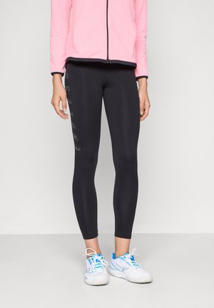 Mujer que lleva leggings negros con el texto "ENDLESS" en la pierna izquierda, zapatillas de running blancas y azules, y una chaqueta rosa con cremallera.