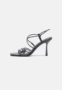 Crne sandale na visokoj potpetici imaju tanke trake s čvorastim dizajnom, glatki kvadratni vrh i elegantnu stiletto petu.