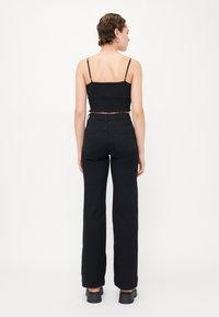 Čierny krátky top s textúrovanou látkou, kombinovaný s vysokými čiernymi širokými nohavicami. Model má na sebe čierne robustné topánky s minimalistickým dizajnom.