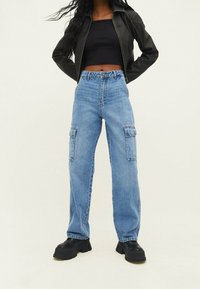 Pantalones cargo de mezclilla azul claro con una cintura alta, dos bolsillos laterales y un ajuste holgado. Combinados con un top negro corto y zapatos de plataforma negros.