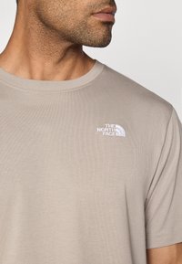 Μπεζ βαμβακερό μπλουζάκι με κοντά μανίκια, με λευκό κεντητό λογότυπο στο αριστερό στήθος. Ομαλή υφή και στρογγυλή λαιμόκοψη.