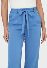 Pantalon bleu clair en tissu texturé, doté d'une ceinture nouée, de poches latérales et d'une coupe ample pour le confort et la liberté de mouvement.