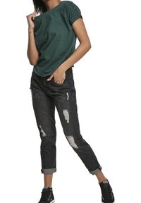 Zeleno-černý pruhovaný tričko, volný střih, v kombinaci s worn-out černými džíny, ohrnutými nad kotníkem, nošené s černými teniskami.