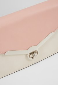 Porte-monnaie en cuir rose et beige avec un fermoir en métal argenté et une décoration sur fond blanc.