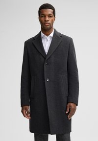Grijze wollen jas met een geknipt kraag, twee voork ску eu一些 и单扣闭合, gedragen over een wit shirt, met een gestructureerd stoffen oppervlak.