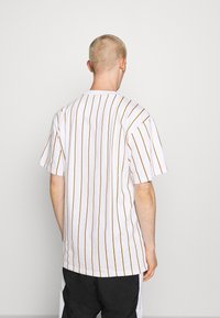 Camiseta blanca de manga corta con rayas verticales marrones, corte relajado, material de algodón, cuello redondo y diseño minimalista.