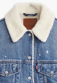 Džínová bunda s beránkovým límcem, modré tkaniny, vybledlými místy a stříbrnými patentkami, s červenou nášivkou Levi's na kapse.