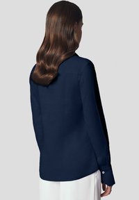 Granatowa koszula z długim rękawem, wykonana z gładkiego materiału, z klasycznym kołnierzykiem i zapinanymi mankietami. Posiada dopasowany krój oraz zaokrąglony dół.