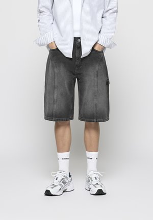 Grijze denimshorts met een losse pasvorm, voorzien van cargozakken en contrasterende stiksels. Gepaard met witte sokken en sneakers.