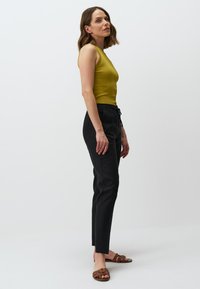 Mouwloze mosterdkleurige top gecombineerd met zwarte taps toelopende broek. Benadrukt met een band met trekkoord en bruine sandalen met banden. Glad textuur door het geheel.
