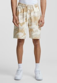 Shorts camouflés en beige et crème, fabriqués en tissu doux. Dotés d'une taille élastique avec cordon de serrage et de poches latérales.