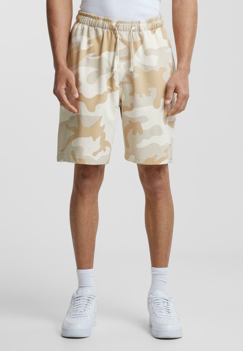 Shorts camouflés en beige et crème, fabriqués en tissu doux. Dotés d'une taille élastique avec cordon de serrage et de poches latérales.