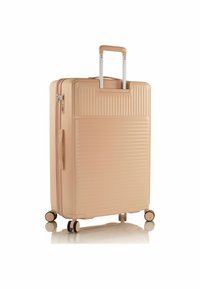 Valise rigide de couleur pêche clair avec texture rainurée verticale, poignée rétractable et quatre roulettes pivotantes pour une mobilité aisée.