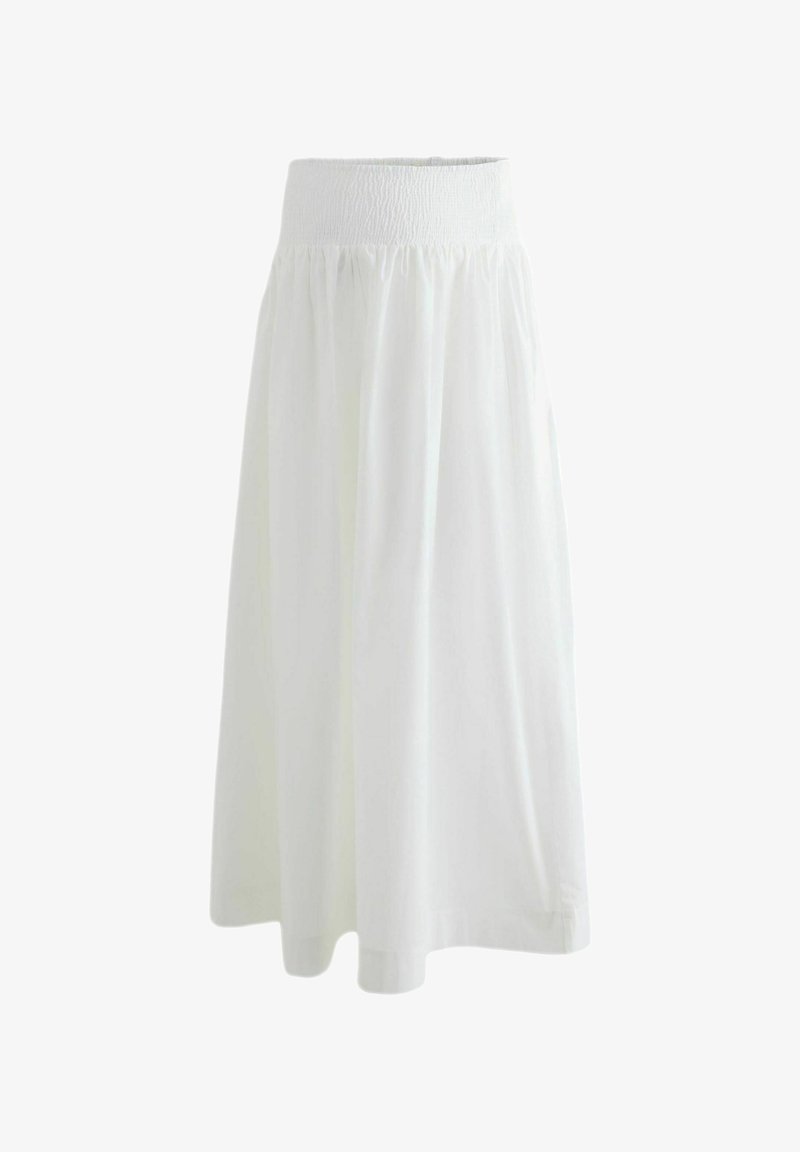 Longue jupe blanche avec une large ceinture smockée et un tissu fluide tombant jusqu'à mi-mollet sur un fond uni.
