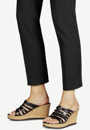 Sandales compensées en cuir noir avec plusieurs lanières verticales, plateforme tressée style jute, design à bout ouvert, portées avec un pantalon tapered noir.