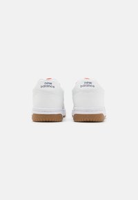Bílé tenisky s gumovou podrážkou, s hladkým koženým svrškem, polstrovaným límcem a logem "new balance" v šedé barvě na patě.