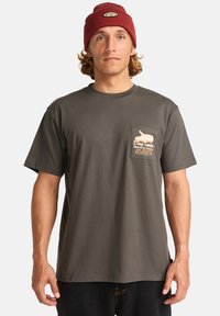 Camiseta de algodón gris oscuro con cuello redondo, mangas cortas y un bolsillo en el pecho izquierdo que presenta un diseño gráfico y texto.