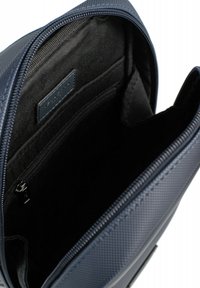 Interno di uno zaino in tessuto blu navy con fodera nera liscia, dotato di una tasca con zip e un'etichetta di lato.