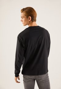 Črna majica z dolgimi rokavi iz bombaža. Okrgla izrez in oprijeti rokavi. Nošena s sivimi kavbojkami. Gladek tekstura, brez vidnih vzorcev.