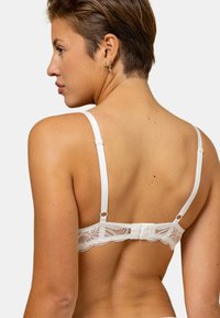 Bralette en dentelle blanche avec des bretelles ajustables, une texture douce et un design à bords festonnés. Fermeture arrière avec crochets et œillet.