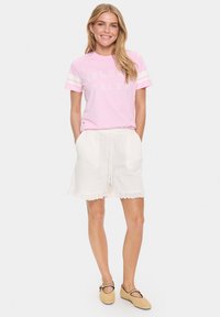 Hellrosa T-Shirt mit weißem "ISLAND TALES" Druck und gestreiften Ärmeln, kombiniert mit weißen Shorts mit Spitzenbesatz und einem Kordelzugbund.