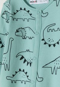 Cardigan verde menta con estampados de dinosaurios negros, con un escote redondo, dos botones y una textura suave y lisa. Ideal para bebés.