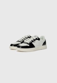 Sneakers bianco e nero in materiale di pelle liscia, con punta perforata e suola in gomma bianca. Presentano il logo del marchio sul lato e un design a contrasto.