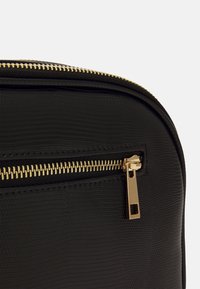 Czarna torebka z ekologicznej skóry o tłoczonej fakturze, z złotym zamkiem błyskawicznym i uchwytem. Zbliżenie na obszar zamka, ukazujące detale.