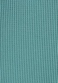 Tela texturizada color verde azulado con patrón de canaletas verticales, acabado suave. El material parece tejido con un espaciado uniforme entre las canaletas, creando un aspecto uniforme.