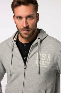Sudadera gris con cremallera frontal, cordones y un logo de "USA Denim". Cuenta con un forro interior a cuadros y un bolsillo a la altura de la cintura.