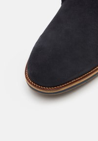 Süße Ankle Boots aus Wildleder in dunkelblau mit einer runden Zehenform, kontrastierenden beigen Nähten und einer strapazierfähigen Sohle mit subtiler Textur.