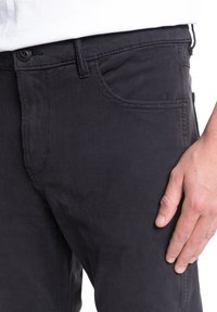 Pantalons en coton noir au design ajusté. Caractéristiques comprenant des poches avant et une fermeture à bouton, présentant une texture lisse et mate.
