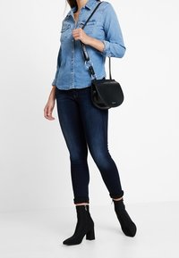 Camisa de mezclilla de color azul claro, jeans ajustados de color azul oscuro, bolso de hombro negro y botines negros con tacón grueso.