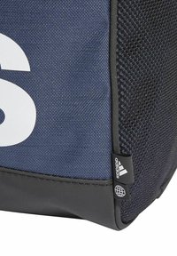 Zaino blu navy con un pannello in rete testurizzata, grande logo bianco e base in gomma nera; presenta un'etichetta di marca sul lato.