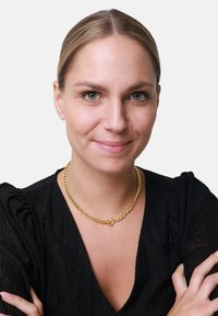 Goldene Kettenhalskette mit einem gedrehten Design, die einen herzf�örmigen Verschluss hat. Über einem schwarzen strukturierten Oberteil getragen, das die Details des Schmucks betont.