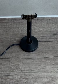 Elektrischer Bart- oder Haarschneider in Schwarz, stehend auf einer runden Ladestation auf einer Holzoberfläche mit grauer Wand im Hintergrund.